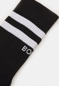Schwarze Baumwollsocke mit zwei weißen horizontalen Streifen und dem Wort "BOLD" in Weiß. Das Material hat eine gerippte Textur.