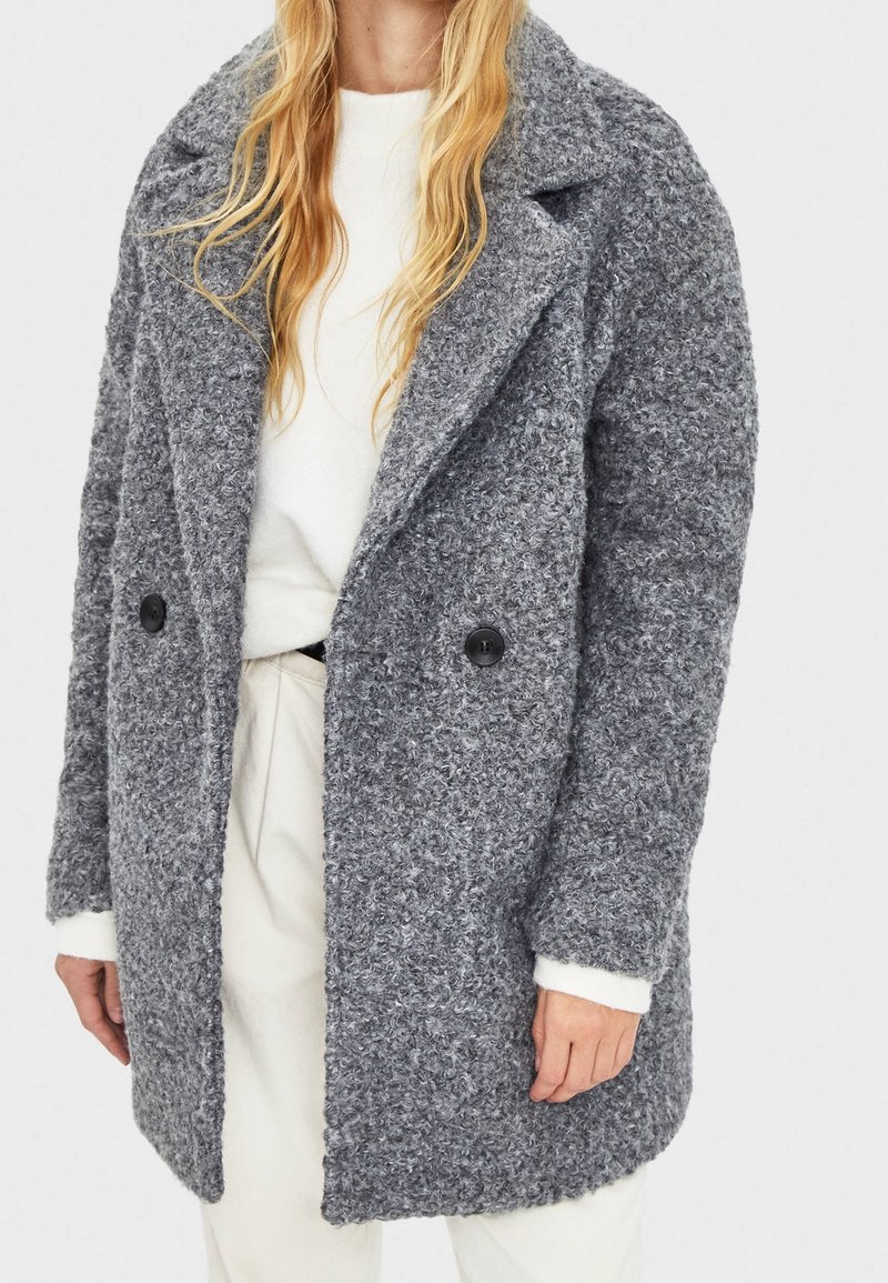 Gray boucle coat with a notched collar, double-button front, and side pockets. Features long sleeves and a textured, cozy material.