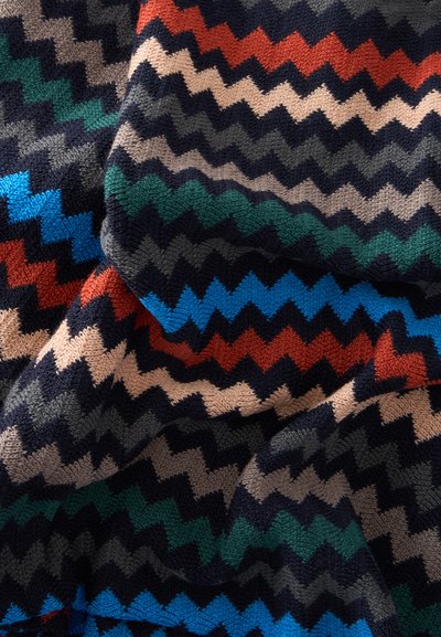 Tissu tricoté avec un motif en zigzag en rouge, bleu, vert, beige, gris et noir, montrant des plis et des détails de texture.
