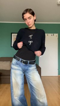 Μαύρο κοντό πλεκτό πουλόβερ με δύο διακοσμητικά ασημένια φιόγκους μπροστά, συνδυασμένο με ανοιχτό μπλε τζιν παντελόνι φαρδιάς γραμμής με ξεθωριασμένη υφή. Περιλαμβάνεται μαύρη ζώνη.