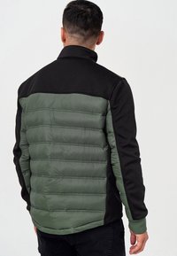 Pikowana kurtka z zielonym pikowanym tułowiem i czarnymi rękawami z tkaniny, z wysokim kołnierzem i ściągaczami na mankietach dla pewnego dopasowania.