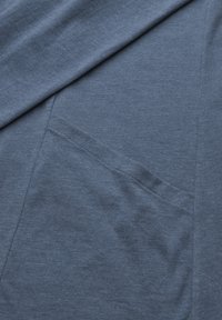 Blauer Baumwollstoff mit einer glatten Textur. Verfügt über eine Tasche mit verstärkten Nähten. Nahaufnahme des Materials und der Form.