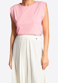 Donna che indossa un top rosa senza maniche infilato in una gonna plissettata bianca a vita alta con una cintura intrecciata.