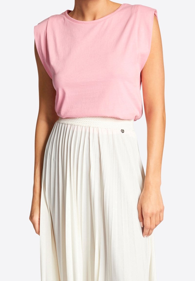 Donna che indossa un top rosa senza maniche infilato in una gonna plissettata bianca a vita alta con una cintura intrecciata.