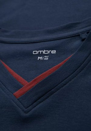 Marineblåt stof med en struktureret overflade har en v-halsdesign. En rød diagonalt streg fremhæver kraven. Mærket siger "ombre M1 eur 48."