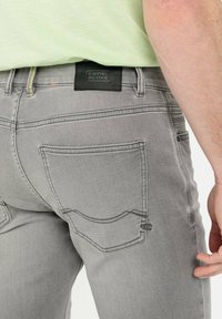 Graue Jeans aus Denim mit schmaler Passform, ausgestattet mit Gesäßtaschen mit kontrastierender Naht und einem schwarzen Lederlabel am Bund.