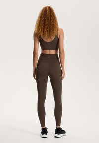 Bézs sportmelltartó és magas derekú leggings rugalmas anyagból, sima textúrával, hátsó logóval és bokáig érő kialakítással.