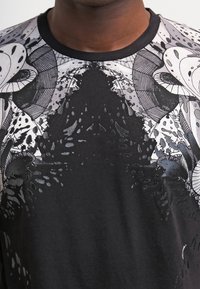 Svart bomull T-shirt med intrikata grå och vita grafiska mönster med organiska former och texturer över bröstområdet.