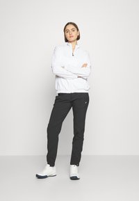 Balta apģērba jaka ar rāvējslēdzēju, ar garām piedurknēm, pārī ar melnām biksēm. Modelis valkā baltas sporta kurpes. Vienkāršs, funkcionāls dizains ar minimāliem akcentiem.