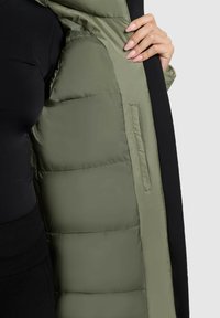 Dūkinis paltas su alyvuogių žalia nailono išorine puse ir juodu pamušalu, su siūtu paminkštinimu ir šoniniu kišeniu.