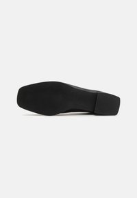 Zwarte platte schoen met een glad leren bovenwerk, vierkante neus en een dikke rubberen zool. De onderkant heeft een gestructureerde grip voor betere tractie.