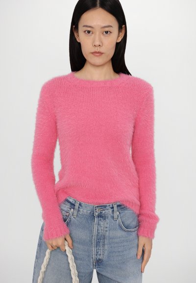 Suéter rosa difuso con cuello redondo y mangas largas, combinado con jeans de mezclilla de cintura alta. El conjunto incluye un bolso trenzado color crema.