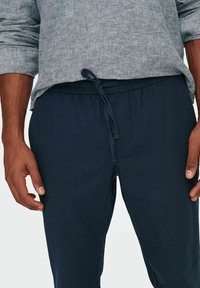 Granatowe spodnie z elastycznym pasem i detalem w postaci sznurka, wykonane z miękkiego materiału, charakteryzujące się luźnym krojem i minimalistycznym designem.