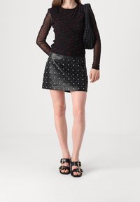 Svart genomskinlig långärmad topp med röda prickar, parat med en svart läder mini kjol med silver nitar, kompletterad med svarta sandaler med spännen.