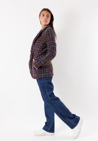 Giacca in tweed multicolore con colletto a scialle e due tasche frontali, abbinata a jeans blu a gamba larga e sneakers bianche.