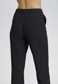 Pantaloni neri in tessuto a maglia con una texture liscia e vita elasticizzata, dotati di tasche laterali e cuciture sartoriali per un aspetto aderente.