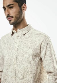 Ljusbeige skjorta med knappar, prydd med ett detaljerat bladmönster, med klassisk krage och mjuk textur.