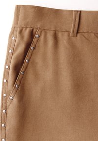 Ruskea kudottu kangas, jossa on sileä pinta ja sivutasku; metalliset niitit korostavat saumaa. Vyötärönauhan muotoilu on yksinkertainen ja jämäkkä.