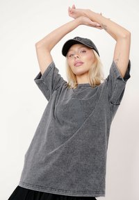 Szara, oversizowa koszulka z krótkimi rękawami i subtelnym nadrukiem. Materiał wydaje się miękki, o fakturowanym wykończeniu. Połączona z szarą czapką.