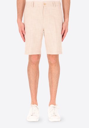 Pantaloncini beige su misura con passanti per cintura, bottone e tasche laterali indossati con sneakers bianche su una persona in piedi su sfondo semplice.