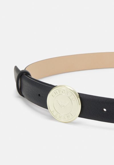 Cinturón de cuero negro con una textura suave, que presenta una hebilla redonda en tono dorado grabada con "Emporio Armani" y detalles del logo.