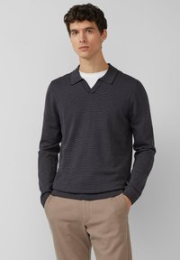 Donkergrijze pullover met V-hals en platte kraag. Heeft lange mouwen en een geribde zoom, gedragen over een wit overhemd. Gladde textuur.