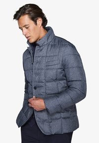 Giacca a vento grigia con un motivo testurizzato, dotata di un colletto alto, chiusura a bottoni e tasche laterali. Materiale morbido e imbottito con un design aderente.