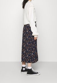 Vit, stickad tröja med voluminösa ärmar som är matchad med en marinblå blommig midi-kjol med orange och vita mönster. Svarta högtoppsskor.