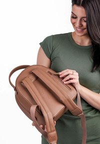 Hnědý kožený batoh s nastavitelnými popruhy, zipovou kapsou na vrchu a hladkým povrchem. Zaoblený design a jemná kovová značka.