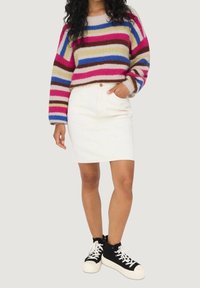 Maglione a maglia multicolore con righe orizzontali in rosa, blu e beige. Abbinato a una gonna di denim bianca e scarpe da ginnastica alte nere.