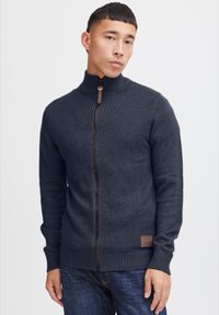 Sweat à fermeture éclair bleu marine foncé avec un motif de tricot texturé, col haut et accent de fermeture éclair marron. Doté d'un écusson logo près de l'ourlet.