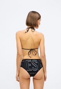 Μαύρο μπικίνι σετ με ρυθμιζόμενο άνοιγμα στο λαιμό και ψηλόμεσο σλιπ με μεγάλου μεγέθους εκτύπωση "DIESEL". Απαλή ύφανση, μινιμαλιστική σχεδίαση.