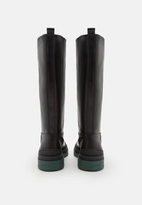 Bottes noires en cuir montant jusqu'aux genoux, à texture lisse, avec une semelle en caoutchouc verte et deux languettes en haut pour faciliter l'enfilage.