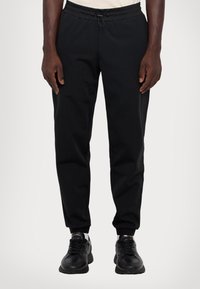 Pantalons de sport noirs avec une taille à cordon de serrage, jambe fuselée et poignets élastiques ; fabriqués en tissu lisse et léger.