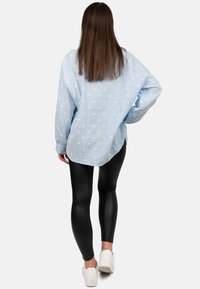 Lichtblauw overhemden met witte stippen, relaxte pasvorm, geweven stof, lange mouwen, gecombineerd met zwarte leggings en witte sneakers.