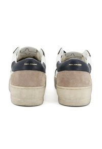 Coppia di sneakers in suede beige e nero con accenti bianchi, segni visibili di usura sulle suole e "AMA-BRAND" in letteratura dorata sui talloni.