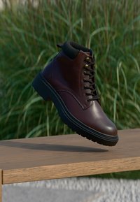 Braune Lederstiefel mit schwarzen Akzenten, runder Zehenpartie und profiliertem Sohlenprofil. Verfügt über Metallösen und Schnürsenkel sowie einen gepolsterten Schaft für zusätzlichen Komfort.