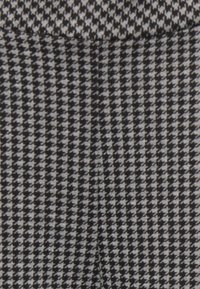 Tecido em padrão pied-de-poule em preto e branco com uma textura suave, apresentando pequenos triângulos que criam um design geométrico repetitivo.