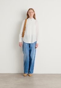 White button-up shirt, loose blue jeans, tan woven shoes, and a brown shoulder bag. Minimalist design with soft textures.