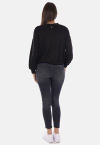 Maglione nero con spalle scese, polsini a coste e dettaglio sul retro. Abbinato a jeans skinny grigio scuro e sneakers bianche.