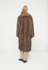 Cappotto in pelliccia sintetica marrone con ampio colletto, maniche lunghe e design fino al ginocchio. Presenta una texture morbida e un fit rilassato.