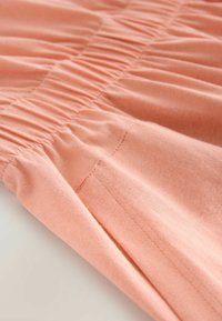 Soft peach fabric with gathered texture. Smooth surface and slight sheen. Seams are neatly finished, highlighting a relaxed design.