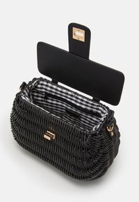 Czarna pleciona torebka o zaokrąglonym kształcie, złote okucia oraz wnętrze w czarno-białą kratę. Posiada klapkę zapinaną na zatrzask.