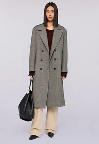 Soprabito in lana grigia con bottoni doppiopetto, ampi risvolti e tasche laterali. Abbinato a pantaloni beige a gamba larga e una borsa nera.