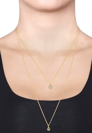 Goldfarbene, geschichtete Halsketten mit einem Herzanhänger und einem Friedenssymbol, beide mit ausgefeilten Designs und feinen Metallketten.
