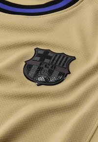 Arany sportmezt cselezett szövettel és fekete FC Barcelona emblémával, csíkozott mintával. Fekete és kék gallérral kiemelve.