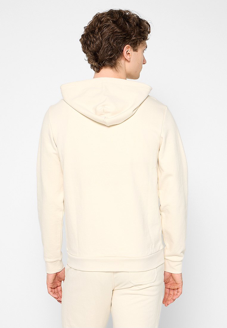 Sweatshirt à capuche de couleur crème avec une texture douce, doté de manches longues, de poignets ribbed et d'une poche kangourou à l'avant.