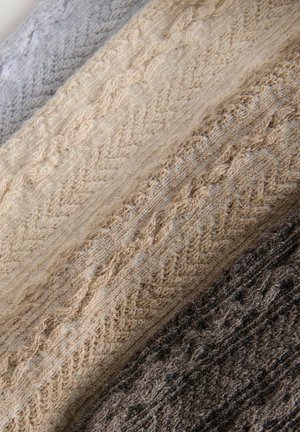 Tissus tricotés dans des nuances de gris, beige et marron, présentant des motifs texturés avec un aspect flou et doux.