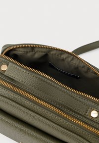 Borsa texture verde oliva con zip dorata, dotata di più scomparti e una fodera interna liscia. Etichetta visibile all'interno.