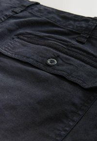 Close-up of navy blue fabric with a buttoned flap pocket and visible stitching on a garment.